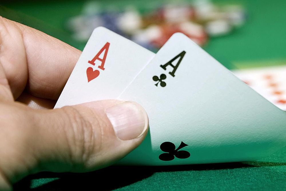 Tangan pemain memegang sepasang kartu As di atas meja poker hijau